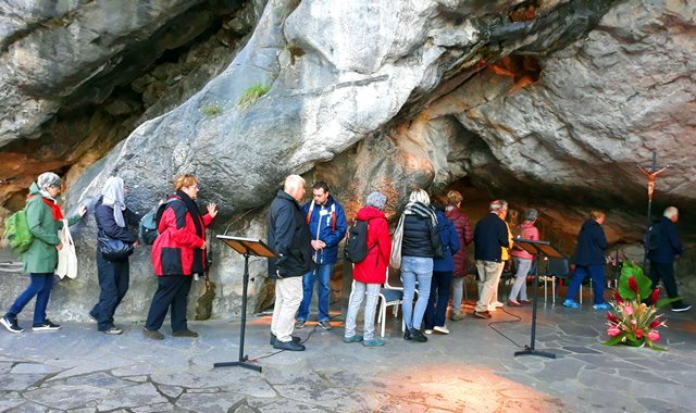 Peregrinos tocam as rochas da Gruta das Aparições no Santuário de Lourdes, na França - foto Viagens de Fé