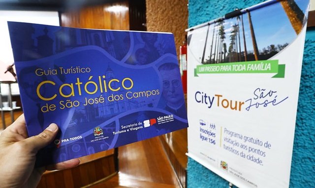 Guia de Turismo Católico de São José dos Campos junto a banner do City Tour oferecido pela cidade - divulgação PMSJC